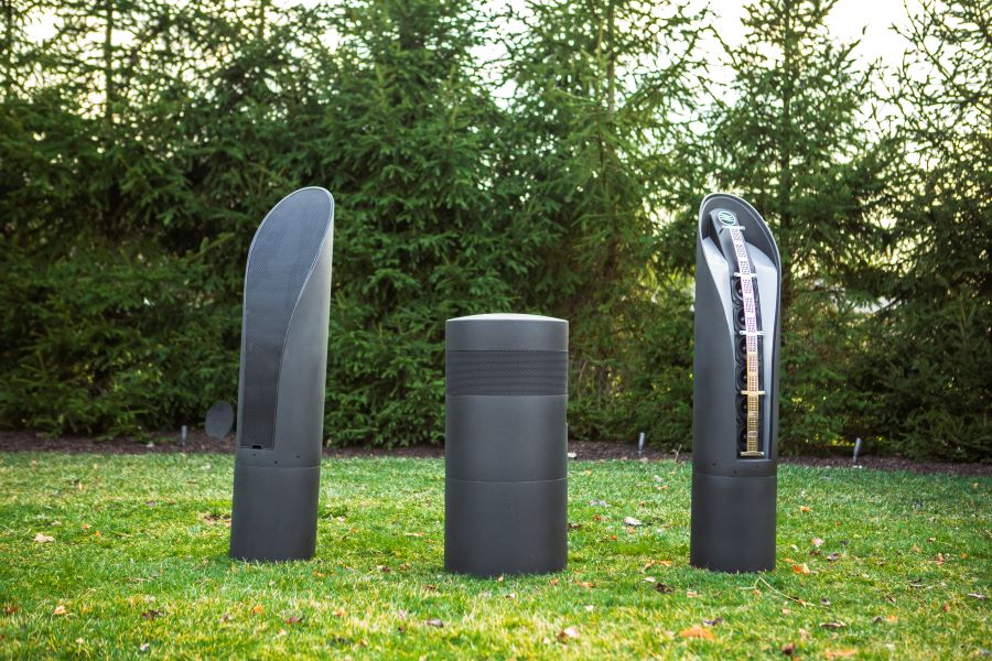 Two of the Coastal Source 12.0 Line Source Bollard speakers, one with the grill on and one with it off, and the 18.0 Subwoofer on a grassy field.