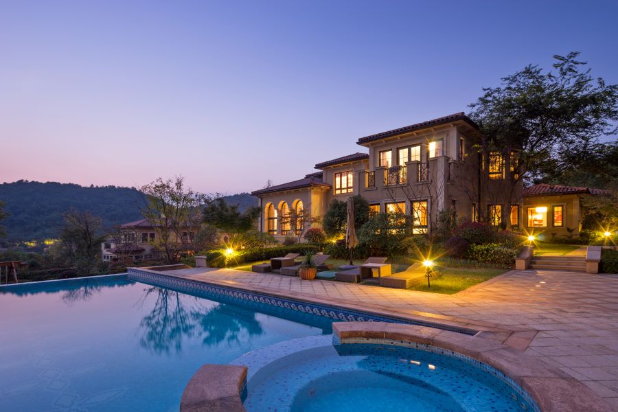 The backyard of a well-lit home with a pool and landscape lighting.